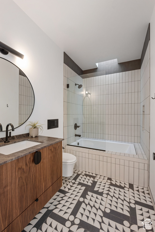 Full bathroom with toilet, tile patterned floors, vanity, and tiled shower / bath