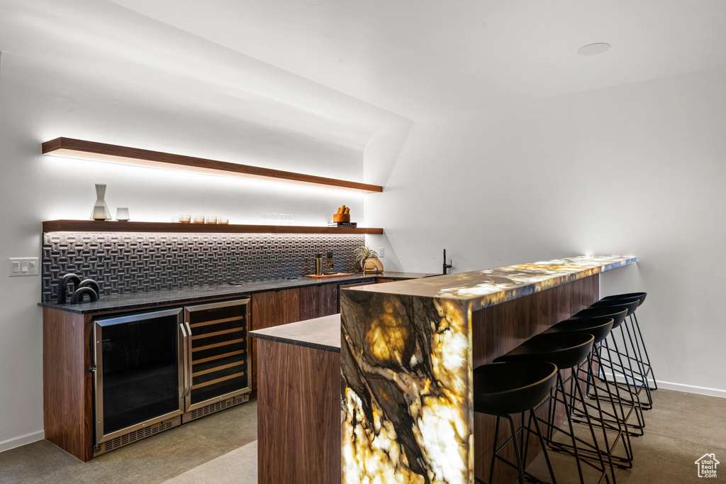Indoor wet bar with wine cooler, light carpet, and backsplash