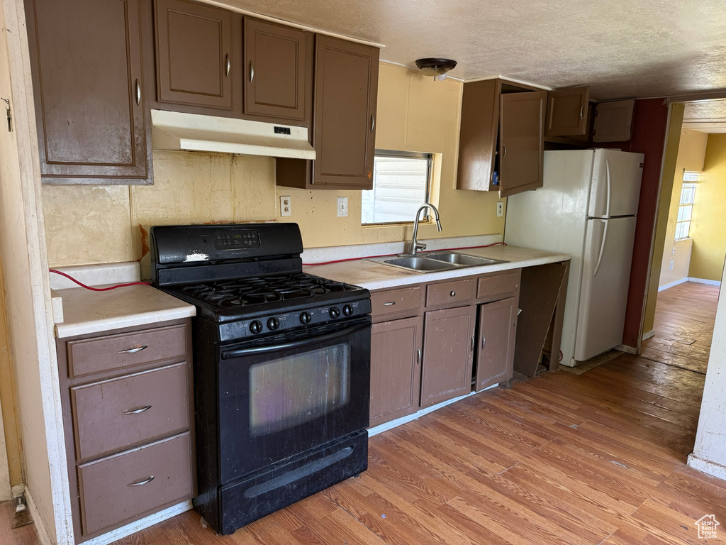 Kitchen with black range with gas stovetop, a sink, under cabinet range hood, light countertops, and a textured ceiling