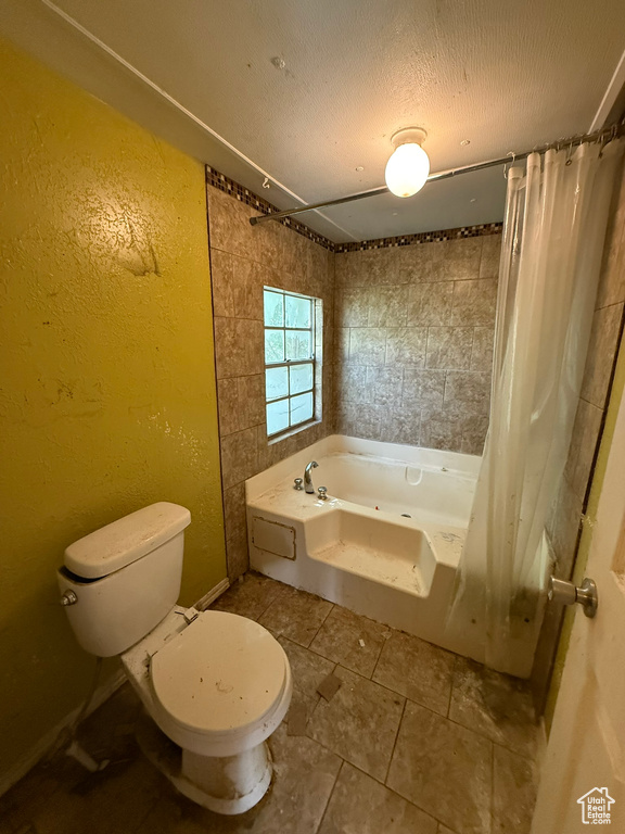 Bathroom with toilet, a combined bath / shower with jetted tub, a textured wall, tile patterned flooring, and a textured ceiling