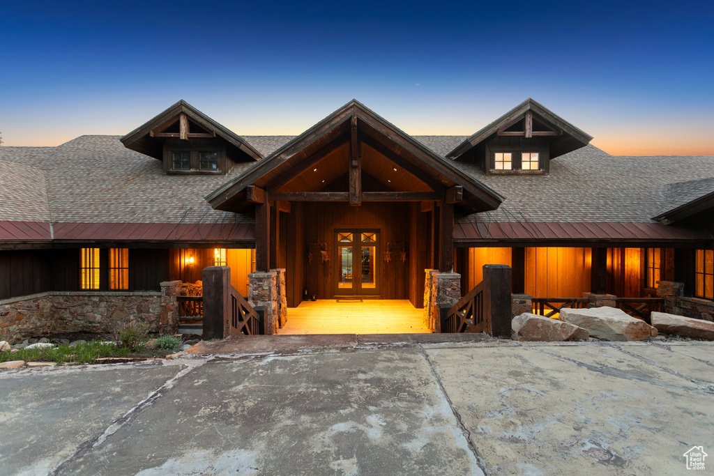 View of front facade featuring french doors, a shingled roof, a porch, and stone siding