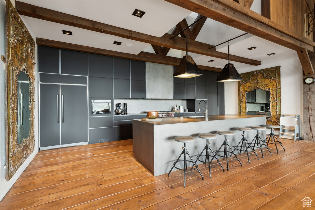 Kitchen with beamed ceiling, light wood-style flooring, a breakfast bar area, modern cabinets, and pendant lighting