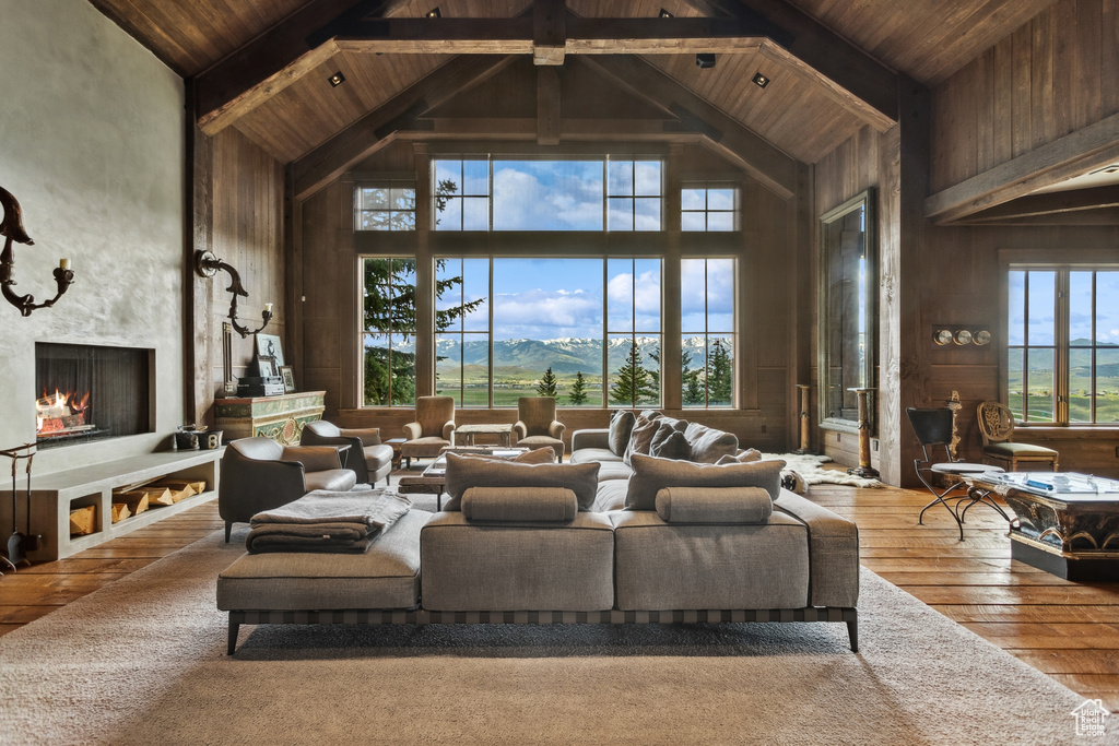 Living area featuring high vaulted ceiling, wooden ceiling with exposed beams, wooden walls, a large fireplace, and hardwood / wood-style floors