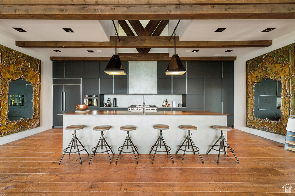 Kitchen featuring light wood-type flooring, a kitchen bar, dark cabinetry, and beamed ceiling