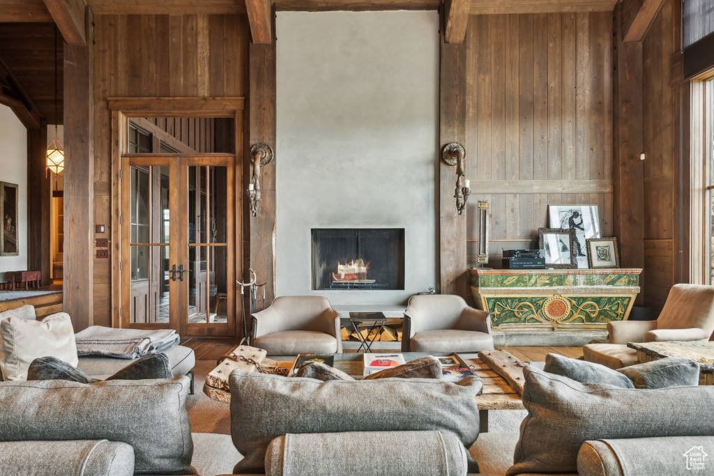 Living room featuring wooden walls, a towering ceiling, wood finished floors, a lit fireplace, and wooden ceiling with exposed beams