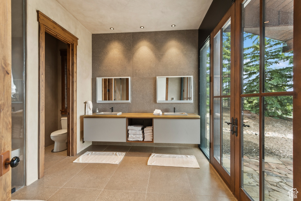 Bathroom featuring double vanity, toilet, french doors, and tile patterned flooring