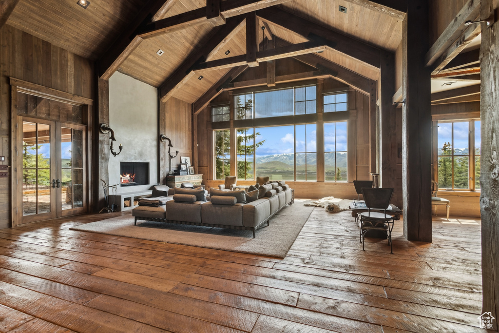 Living area featuring high vaulted ceiling, french doors, hardwood / wood-style floors, wooden ceiling with exposed beams, and a large fireplace