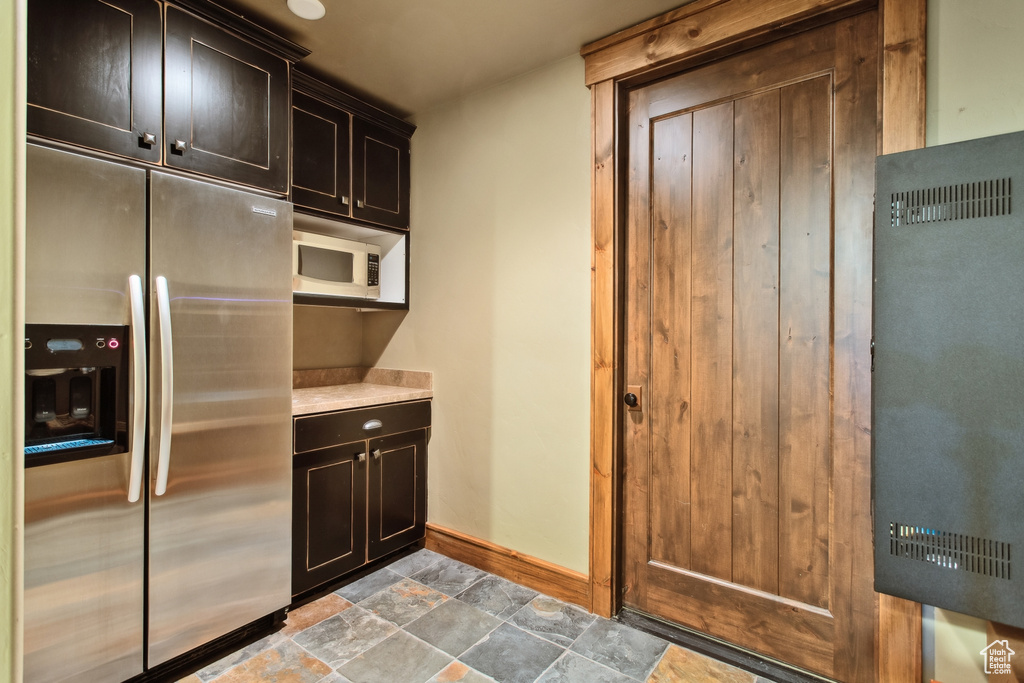 Kitchen featuring stainless steel refrigerator with ice dispenser, white microwave, baseboards, stone finish floors, and light countertops