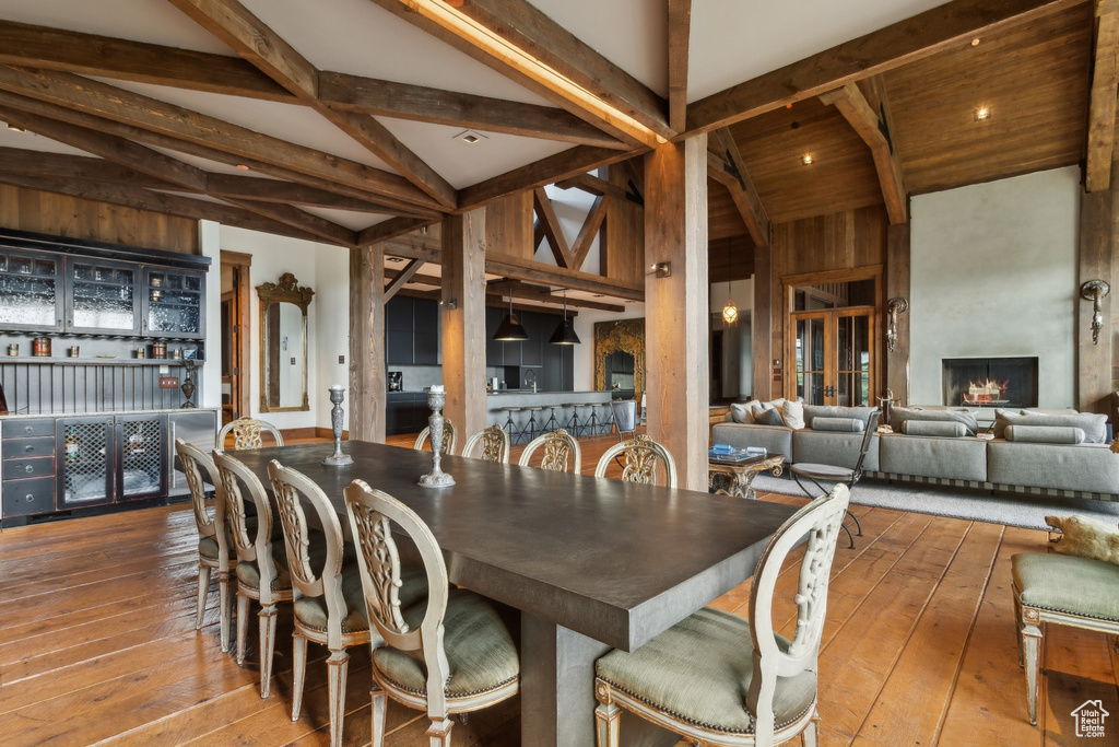 Dining space with hardwood / wood-style floors, beamed ceiling, a large fireplace, and high vaulted ceiling
