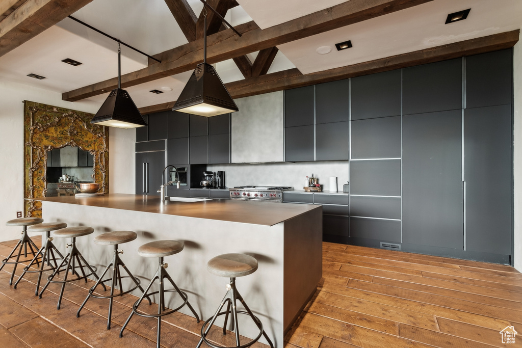 Kitchen featuring beam ceiling, modern cabinets, light wood-style floors, tasteful backsplash, and dark cabinetry