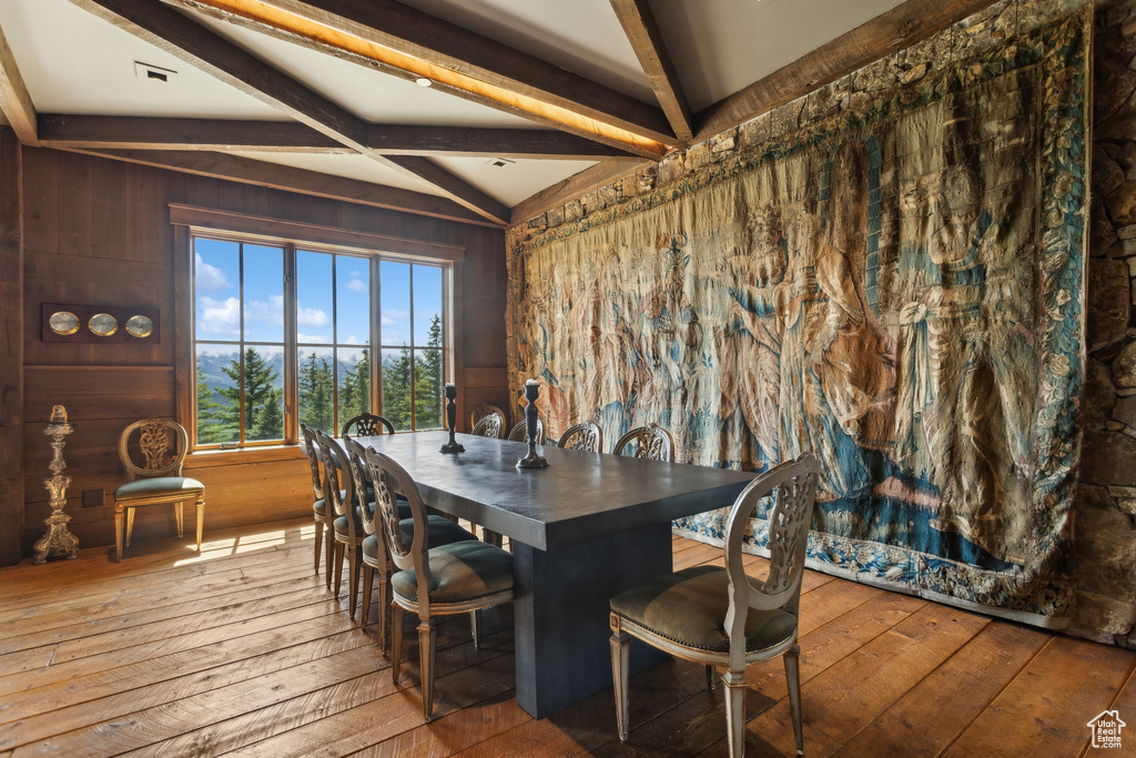 Dining area with hardwood / wood-style floors, beamed ceiling, and wooden walls