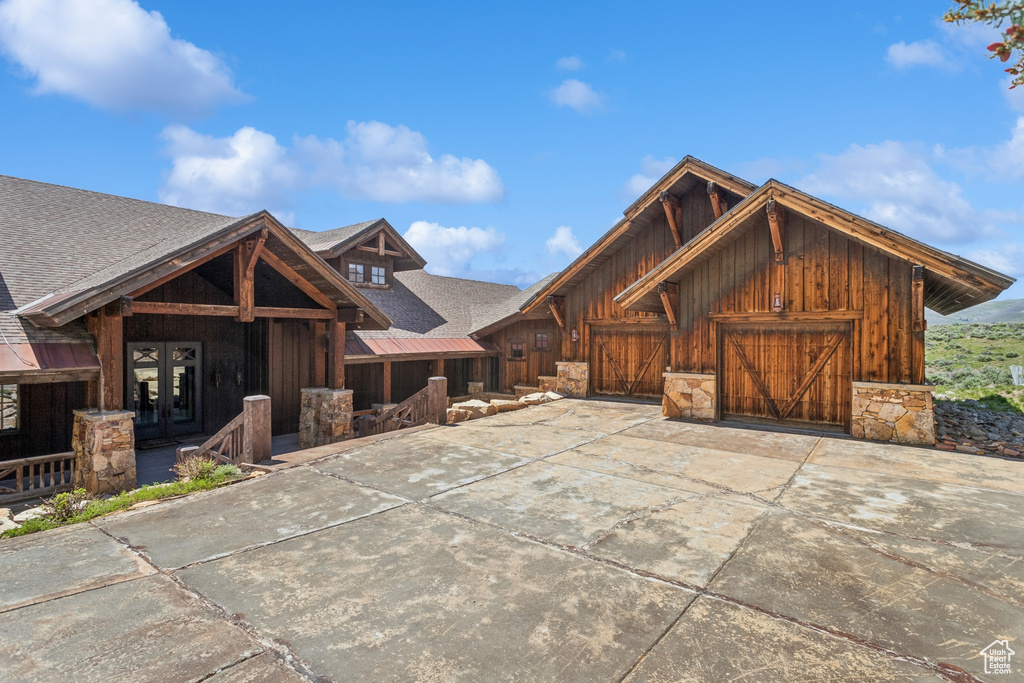 Rustic home with french doors, board and batten siding, roof with shingles, driveway, and an attached garage