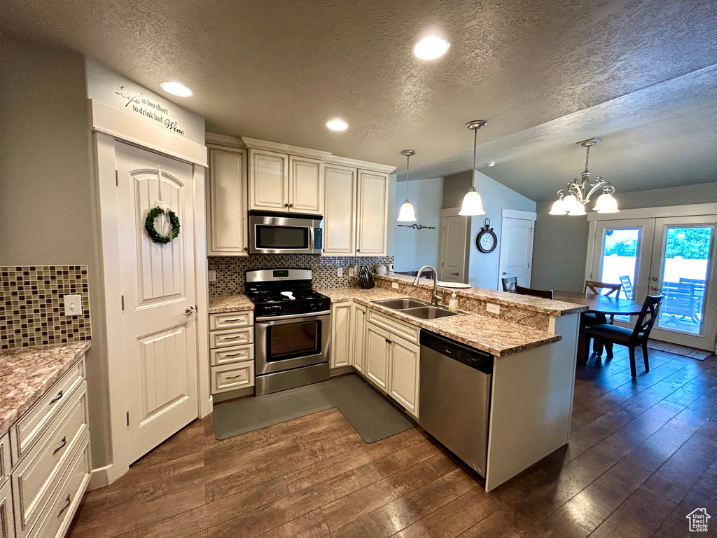 Kitchen with appliances with stainless steel finishes, a sink, a peninsula, a textured ceiling, and vaulted ceiling