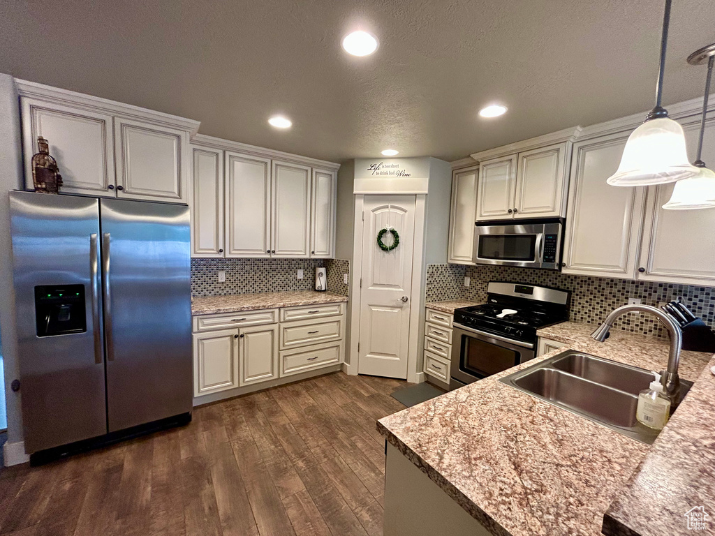 Kitchen with appliances with stainless steel finishes, a sink, dark wood-style flooring, pendant lighting, and decorative backsplash