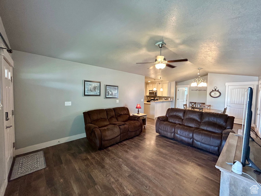 Living area with lofted ceiling, dark wood-type flooring, a chandelier, ceiling fan, and baseboards