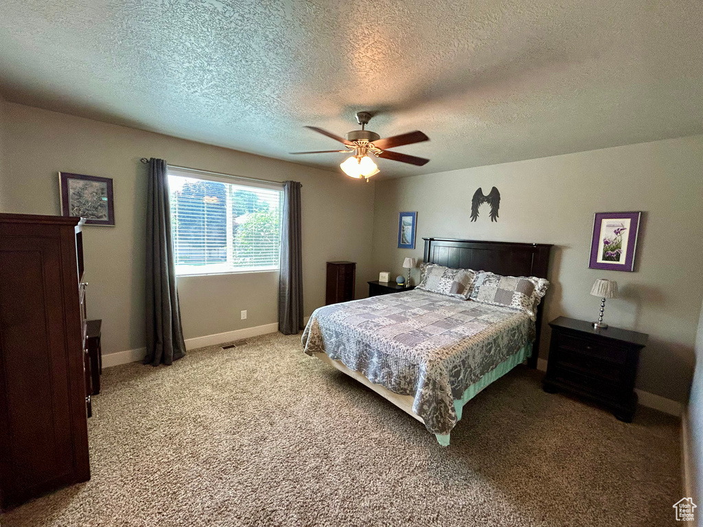 Bedroom with a textured ceiling, light carpet, baseboards, and a ceiling fan