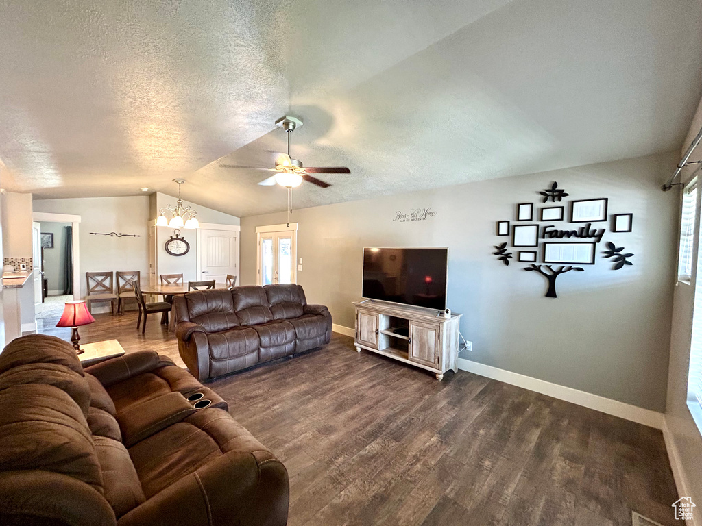 Living room featuring vaulted ceiling, dark wood-style floors, baseboards, a ceiling fan, and a textured ceiling