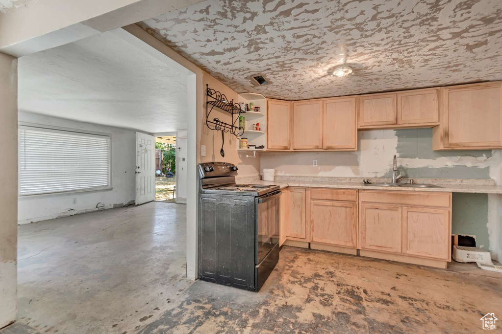 Kitchen with black electric range oven, light brown cabinetry, a sink, and light countertops
