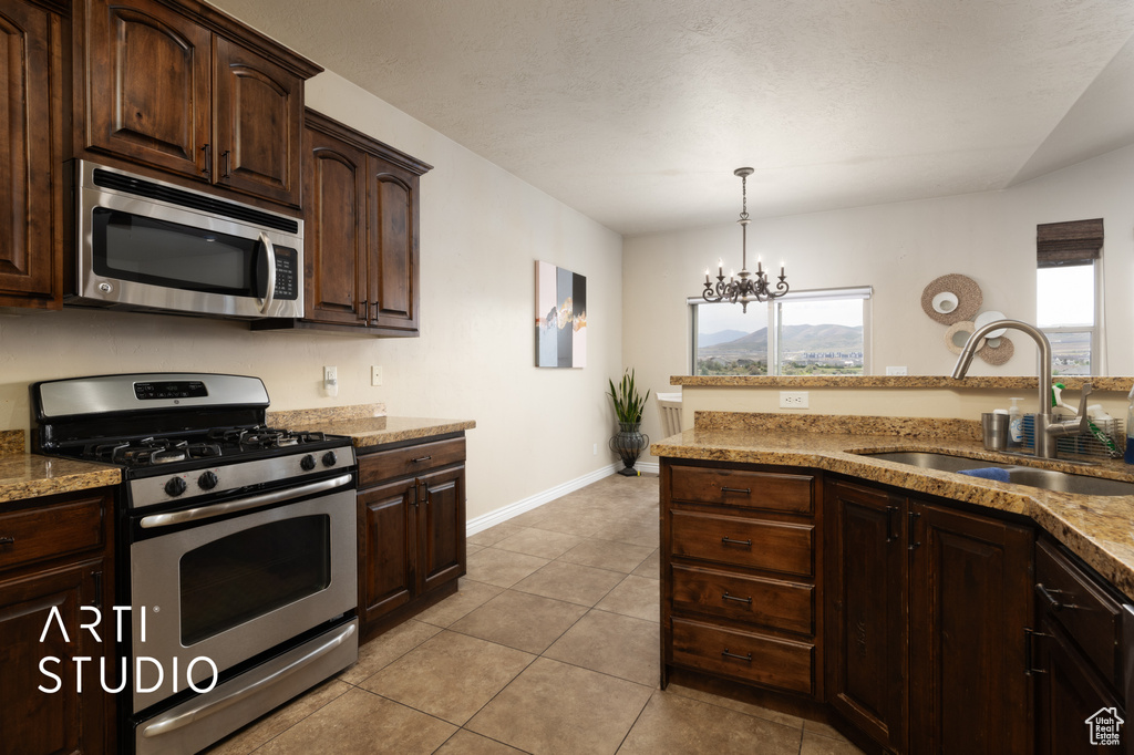 Kitchen featuring stainless steel appliances, a sink, dark brown cabinetry, baseboards, and a chandelier
