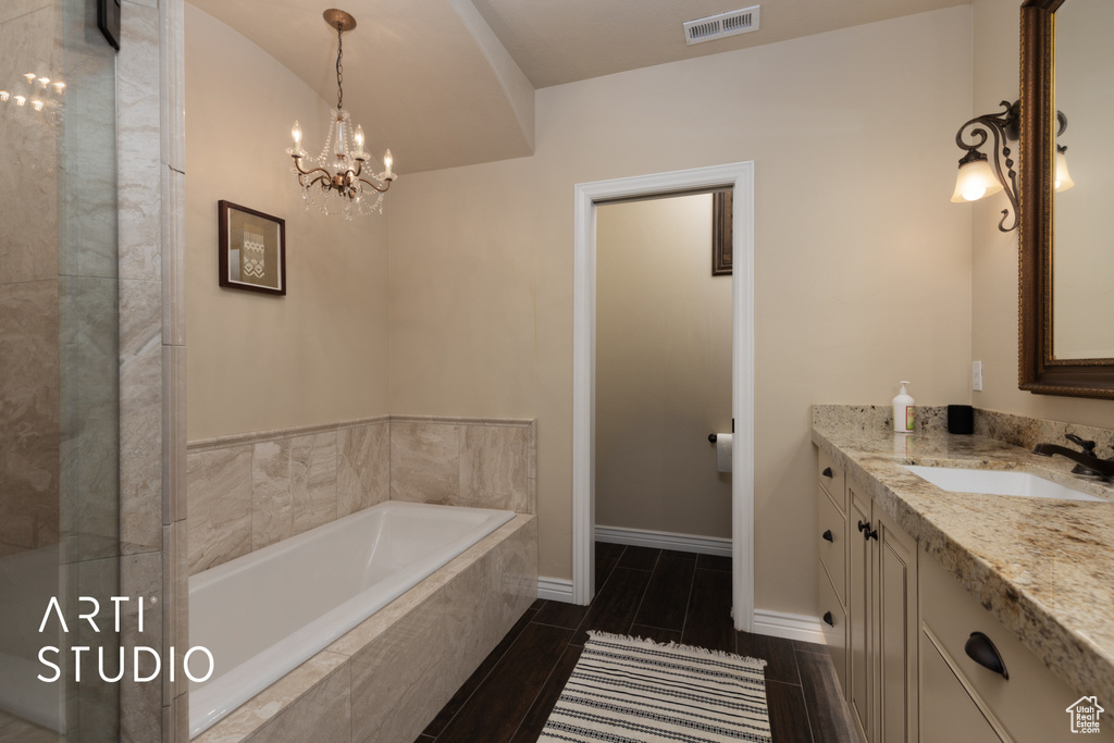 Full bathroom featuring vanity, a bath, a chandelier, and baseboards
