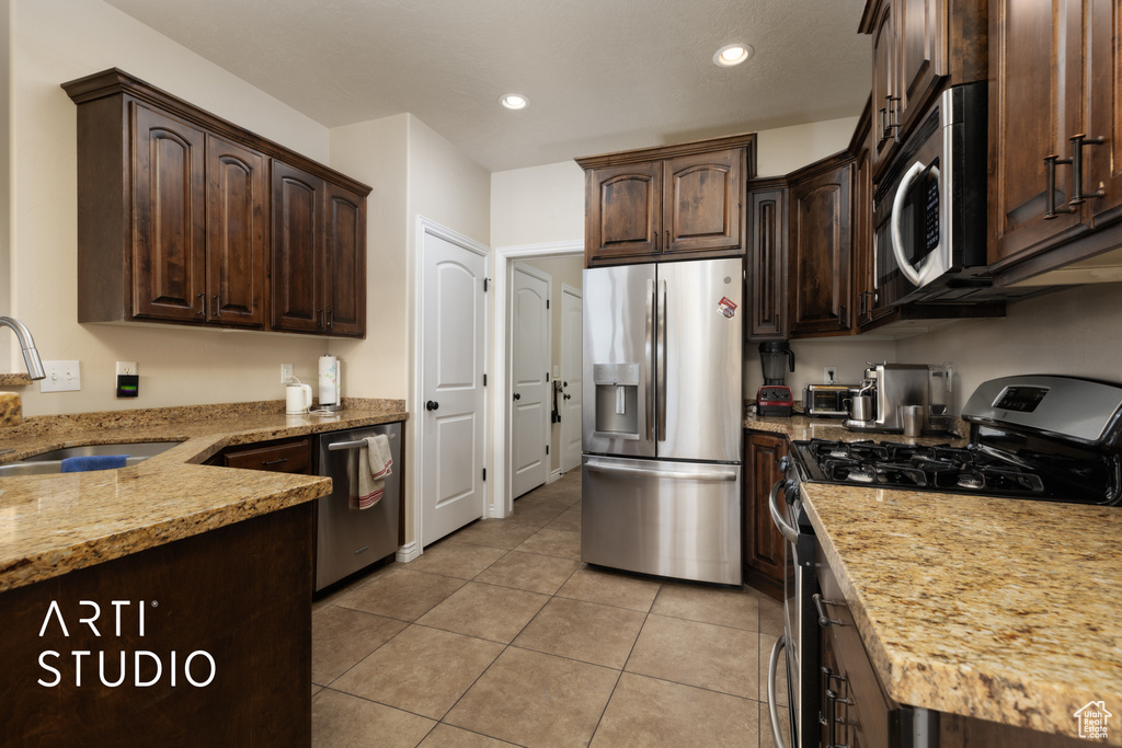 Kitchen featuring stainless steel appliances, a sink, dark brown cabinets, light stone countertops, and light tile patterned floors