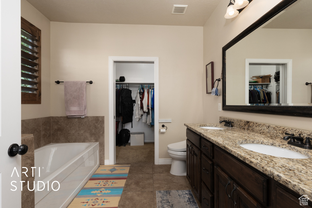 Full bathroom with double vanity, a bath, a walk in closet, toilet, and tile patterned floors