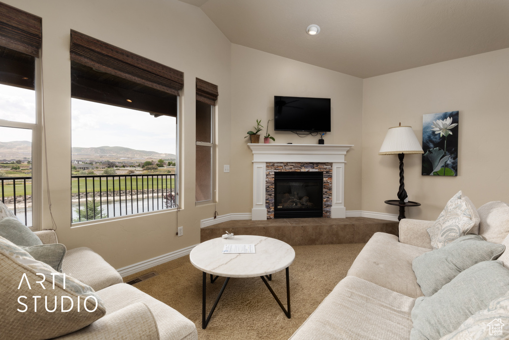 Living room featuring carpet flooring, lofted ceiling, a stone fireplace, and baseboards