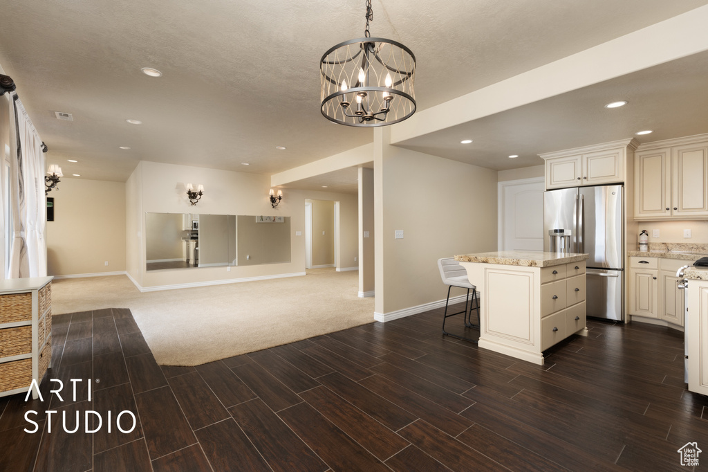 Kitchen featuring stainless steel refrigerator with ice dispenser, wood finish floors, a kitchen island, a kitchen breakfast bar, and baseboards