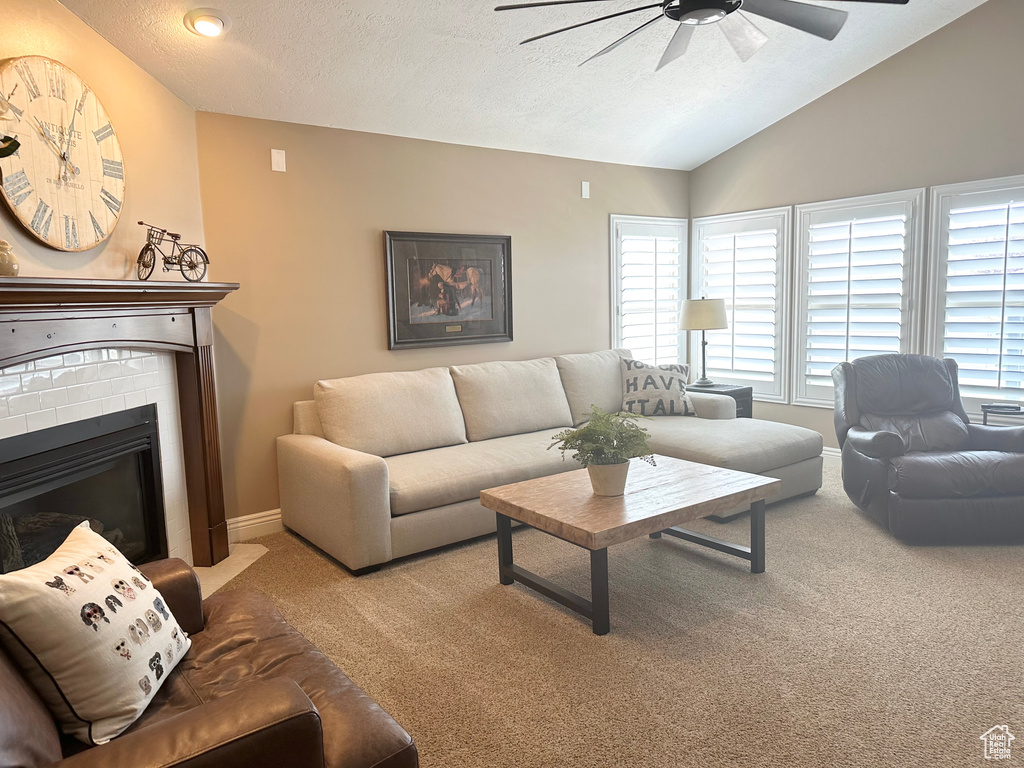 Living room featuring a ceiling fan, lofted ceiling, carpet, a brick fireplace, and a textured ceiling