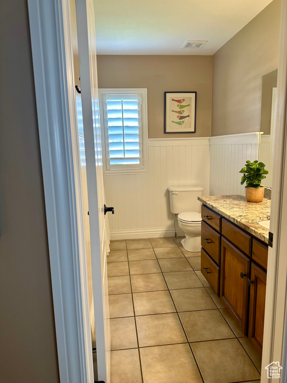 Bathroom featuring toilet, vanity, tile patterned floors, and a wainscoted wall