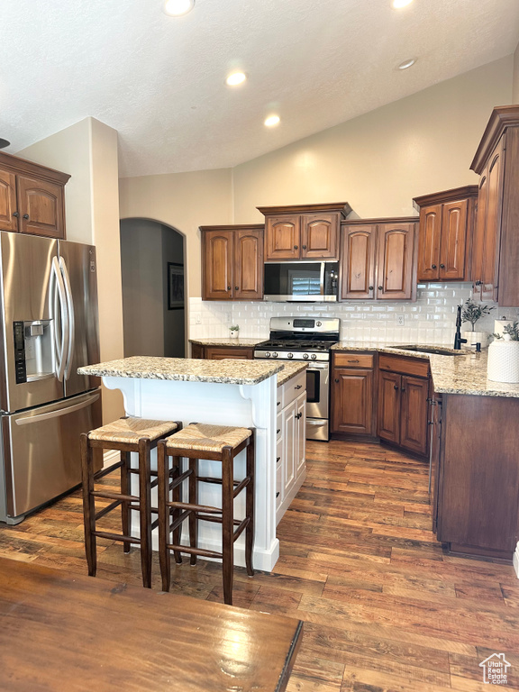 Kitchen featuring stainless steel appliances, arched walkways, a kitchen breakfast bar, tasteful backsplash, and light stone countertops