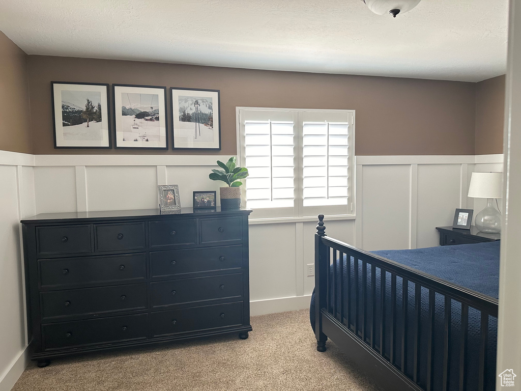 Bedroom featuring a decorative wall, light colored carpet, and a wainscoted wall