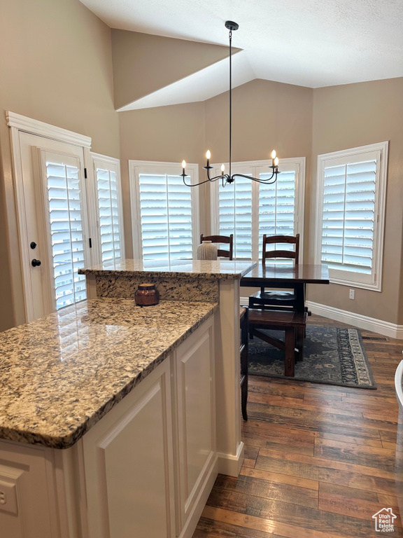 Kitchen with dark wood-style floors, vaulted ceiling, white cabinets, a chandelier, and light stone countertops