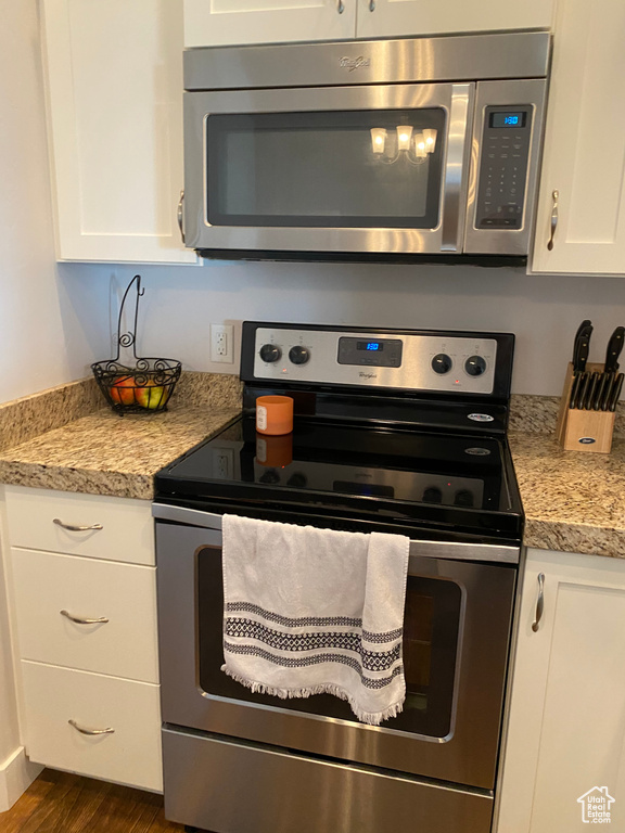 Kitchen with stainless steel appliances, light countertops, white cabinetry, and dark wood finished floors