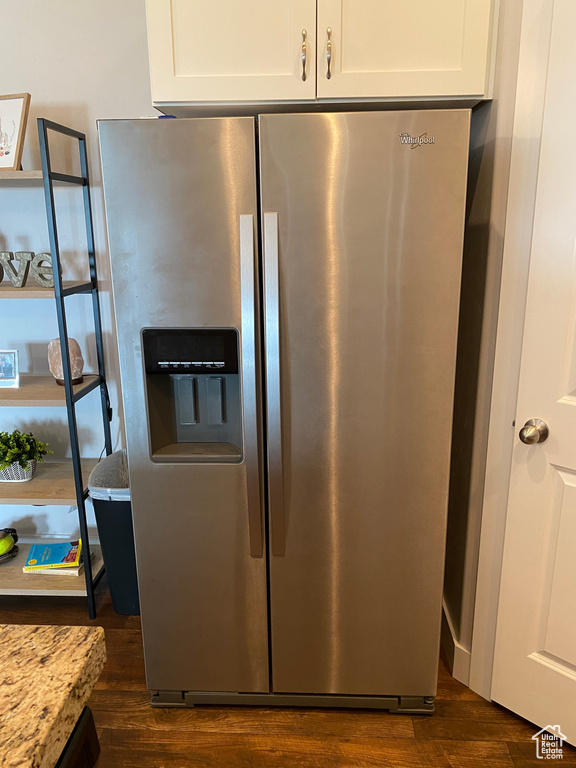 Kitchen view of stainless steel fridge with ice dispenser, dark wood finished floors, white cabinetry, and light stone countertops