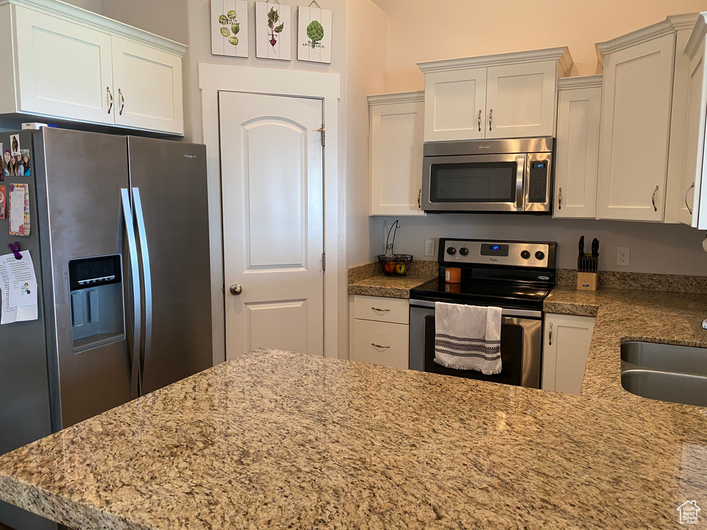 Kitchen with stainless steel appliances, white cabinetry, a sink, and light stone countertops