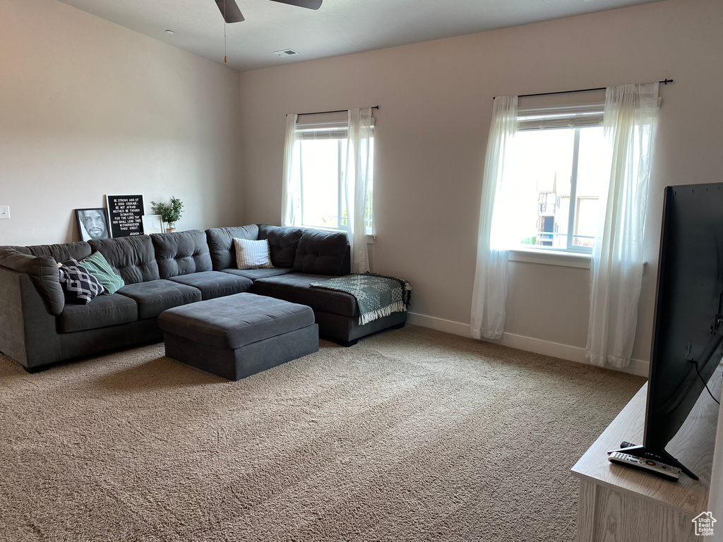 Carpeted living area featuring ceiling fan and baseboards