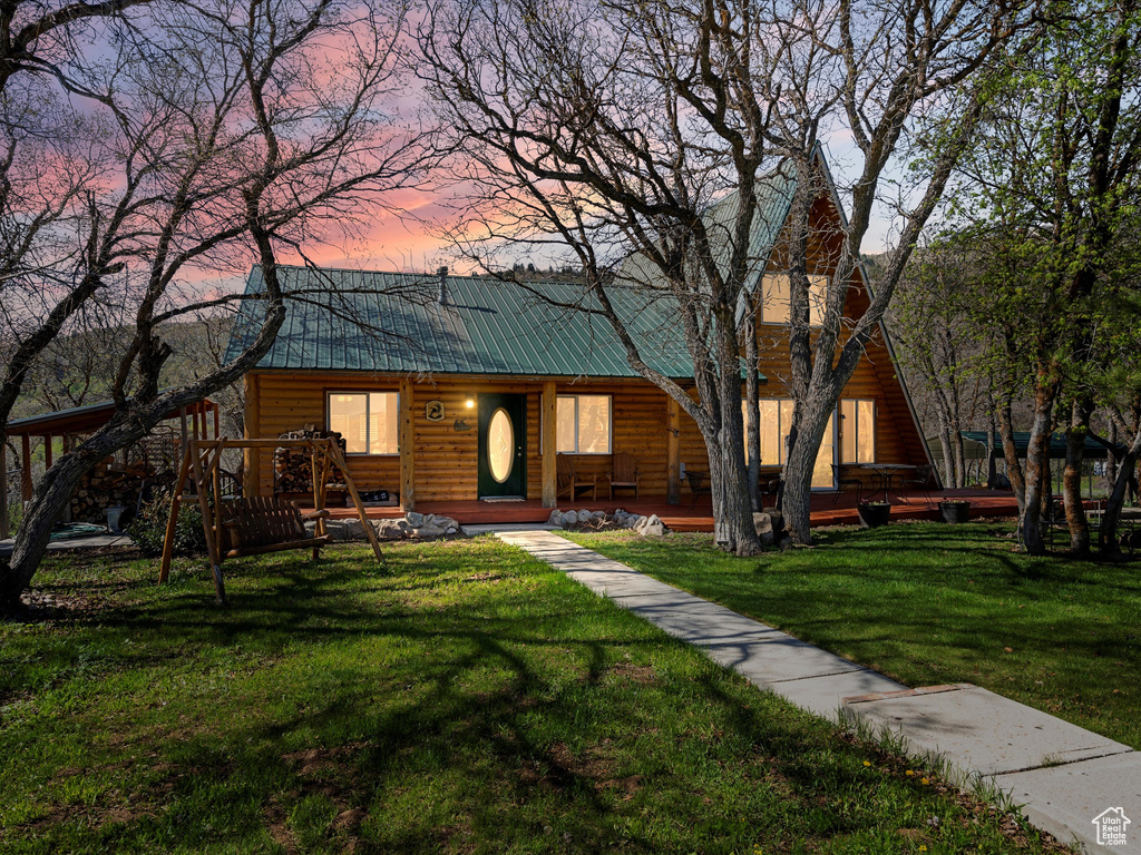 View of front of home with faux log siding, metal roof, a lawn, and a porch