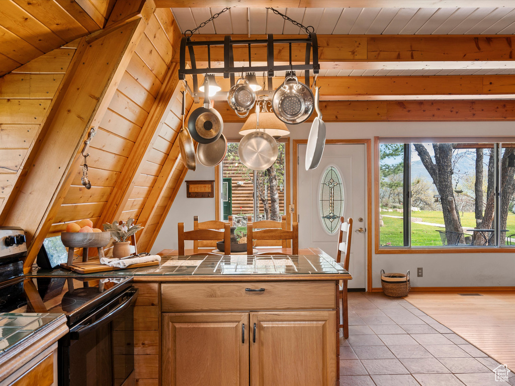 Kitchen with tile countertops, black range with electric cooktop, light tile patterned flooring, wood ceiling with exposed beams, and a chandelier