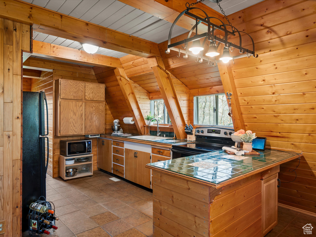 Kitchen featuring electric range, tile countertops, freestanding refrigerator, a sink, and wood walls