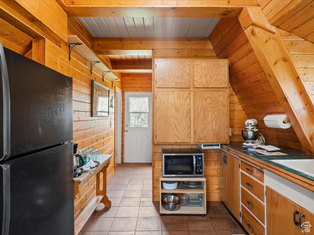 Kitchen featuring freestanding refrigerator, stainless steel microwave, wooden walls, wood ceiling with exposed beams, and tile patterned floors