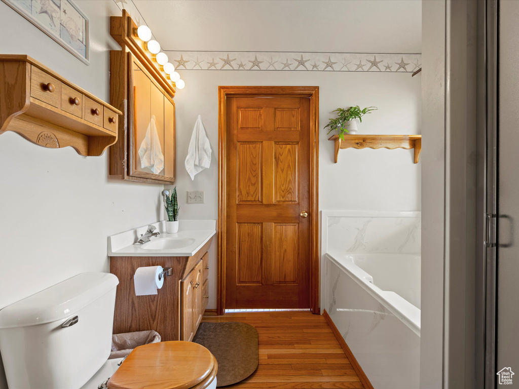 Bathroom featuring vanity, toilet, a garden tub, and wood finished floors