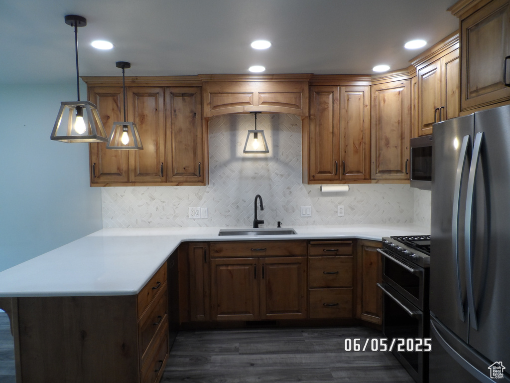 Kitchen featuring stainless steel appliances, a sink, a peninsula, dark wood-type flooring, and backsplash