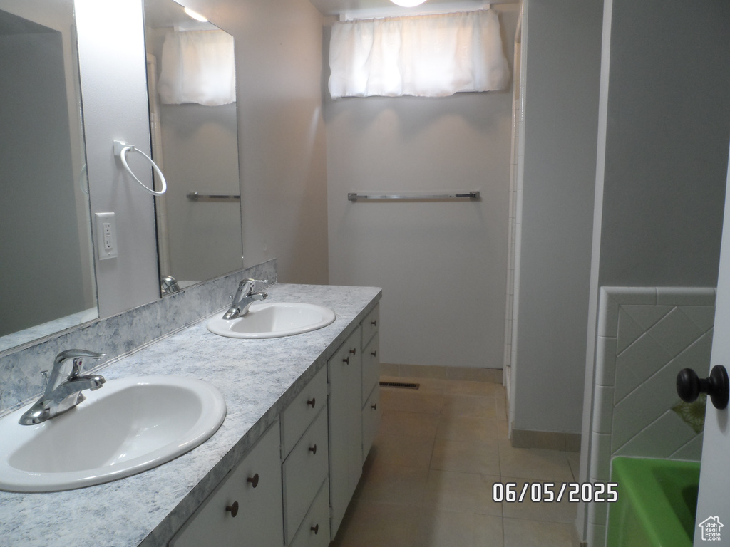 Bathroom featuring double vanity, tile patterned flooring, a tub to relax in, and baseboards