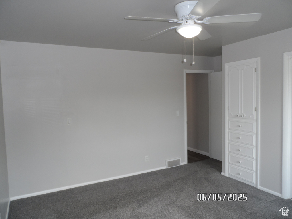 Unfurnished bedroom featuring dark colored carpet, baseboards, and ceiling fan