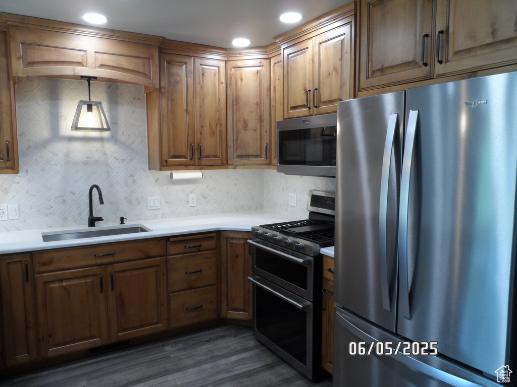 Kitchen featuring stainless steel appliances, a sink, backsplash, dark wood-style floors, and light countertops