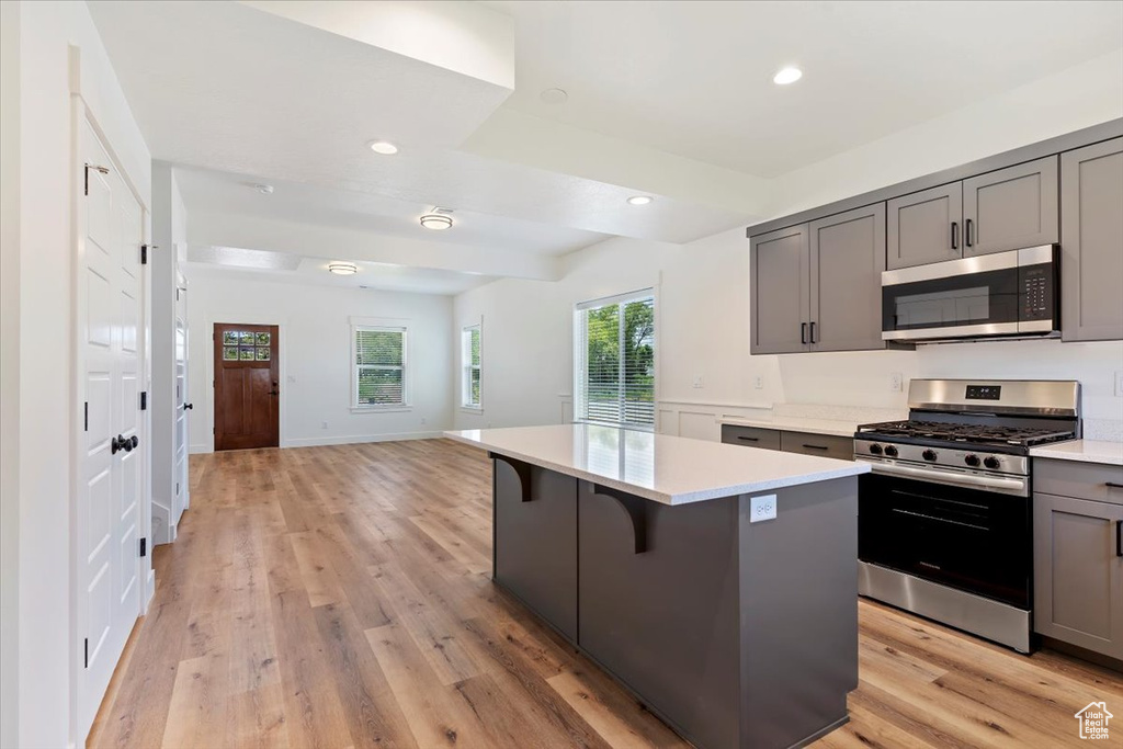 Kitchen featuring appliances with stainless steel finishes, gray cabinets, light countertops, open floor plan, and a center island