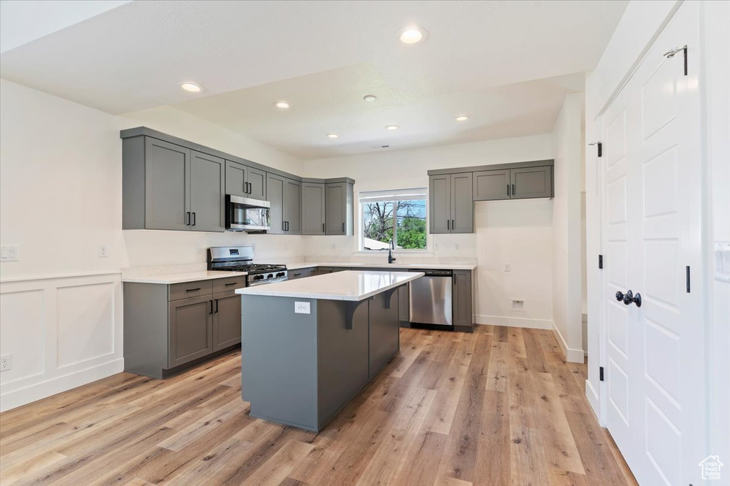 Kitchen featuring appliances with stainless steel finishes, gray cabinetry, a kitchen island, light countertops, and light wood-style flooring