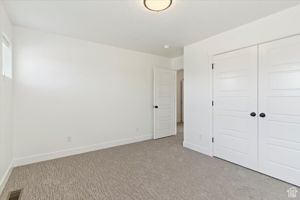 Unfurnished bedroom with light colored carpet, baseboards, and a closet