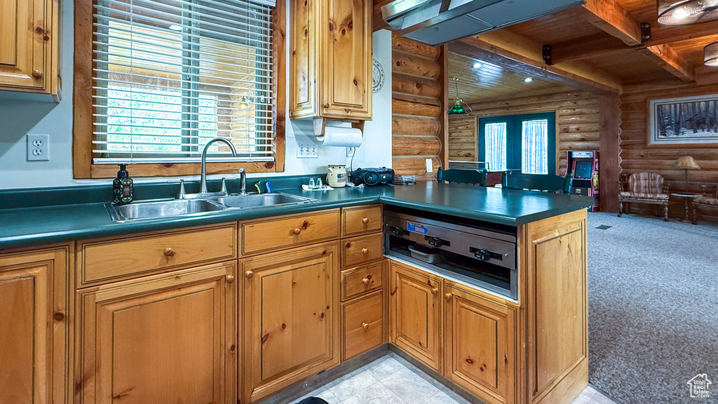 Kitchen with rustic walls, a sink, wooden ceiling with exposed beams, dark countertops, and a peninsula